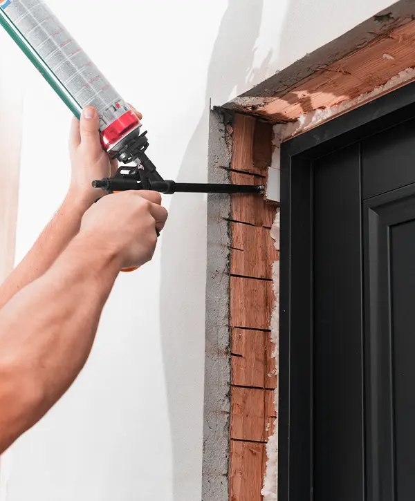 a man sprays construction foam between a new wooden door and a wall