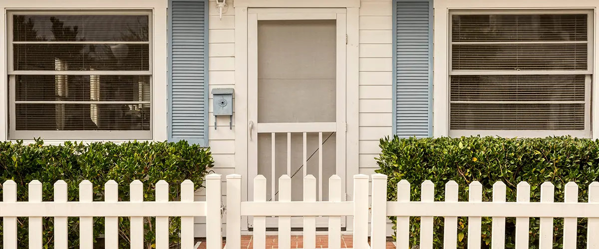 White front door with a screen door surrounded by a white picket fence adorned by string lights.